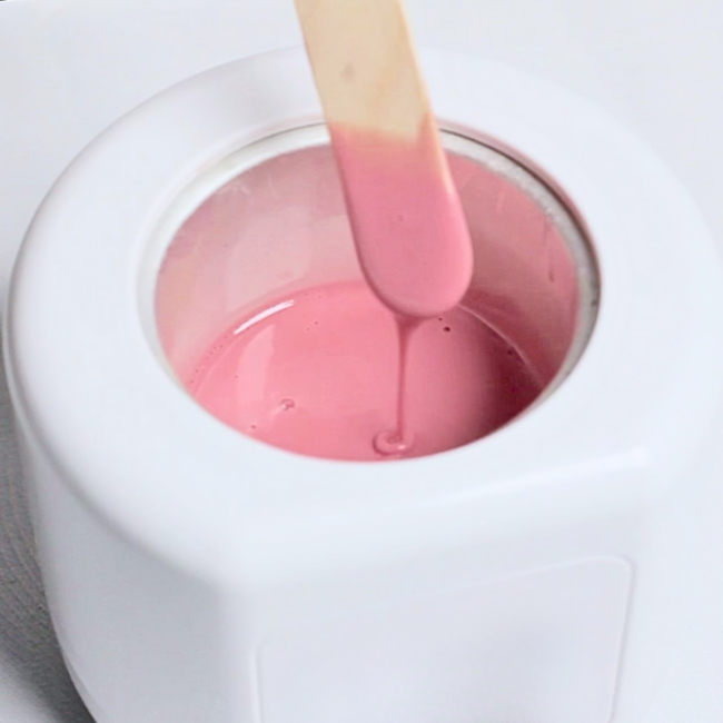 Pink wax melted in warmer with wax stick applicator